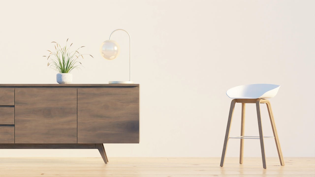 Modern minimalist interior featuring a wooden sideboard, chair, lamp, and plant against a white wall.